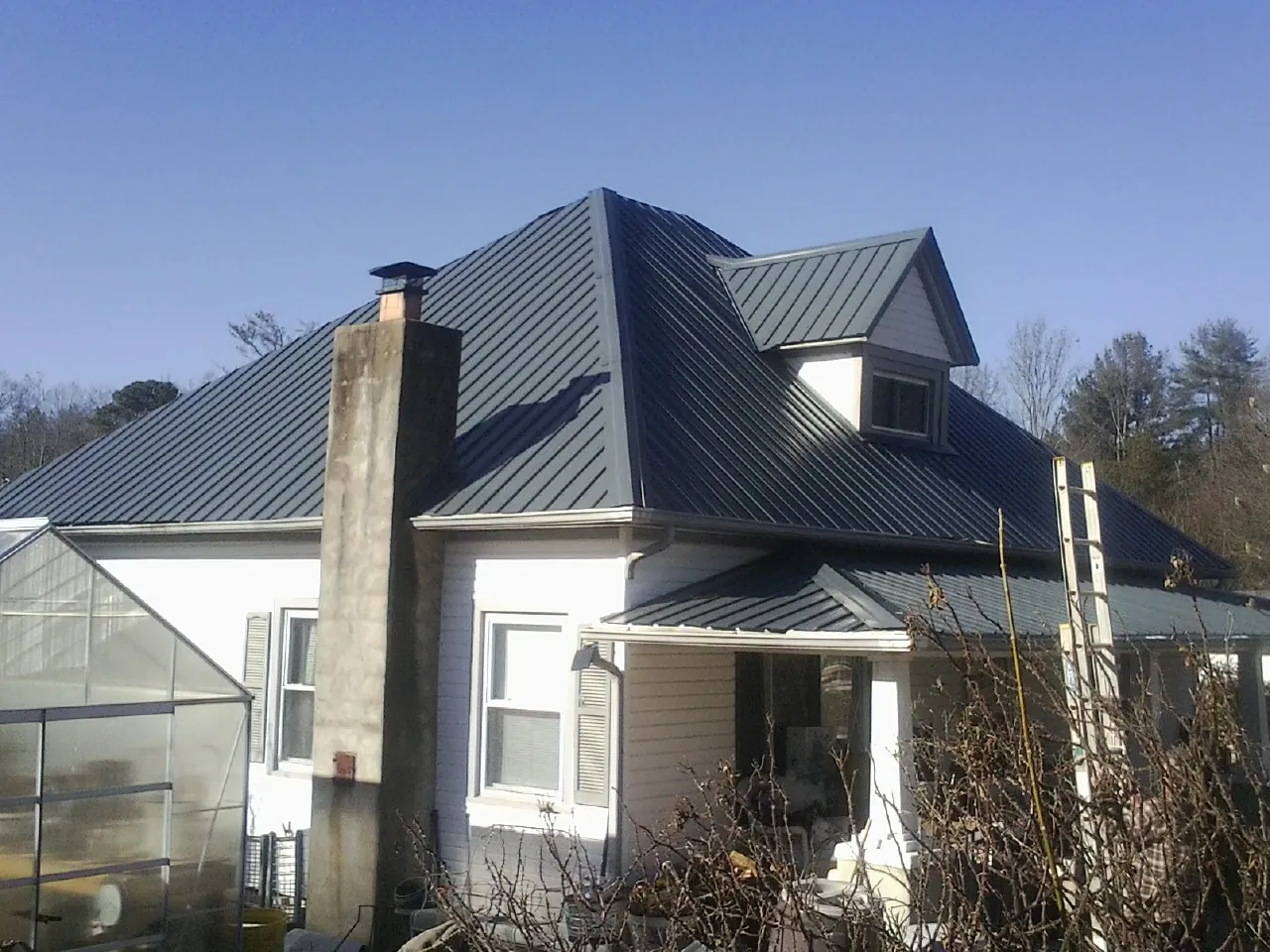 Dark blue standing seam metal roof on a white farmhouse with dormer — Slate & Tile Roof Repair by Roofing Brothers in Bishop Hill