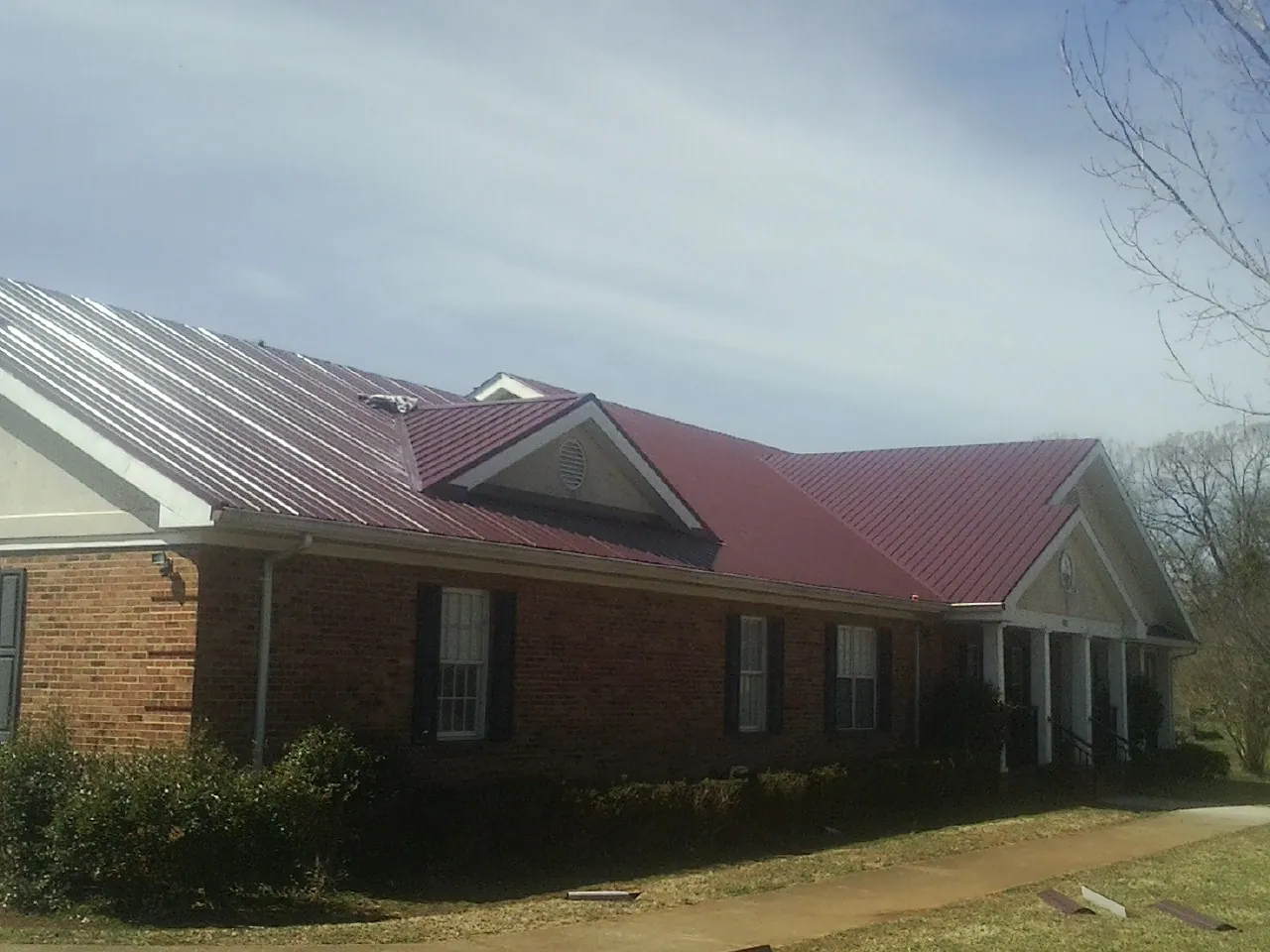 Red metal roof with gabled entries on a long brick building, from a Hail Damage Roof Repair job in Bishop Hill