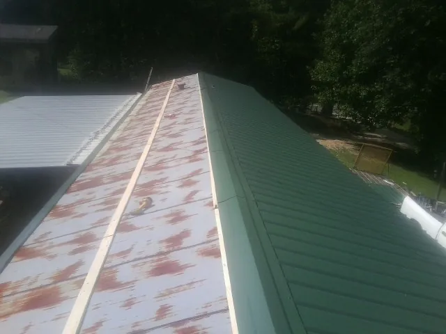 Old rusted panels beside newly installed green metal roofing — Wind Damage Roof Repair by Roofing Brothers in Bishop Hill