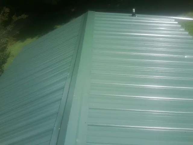 New green metal panels meeting at the ridge of a roof — Flat Roof Repair work by our crew in Bishop Hill