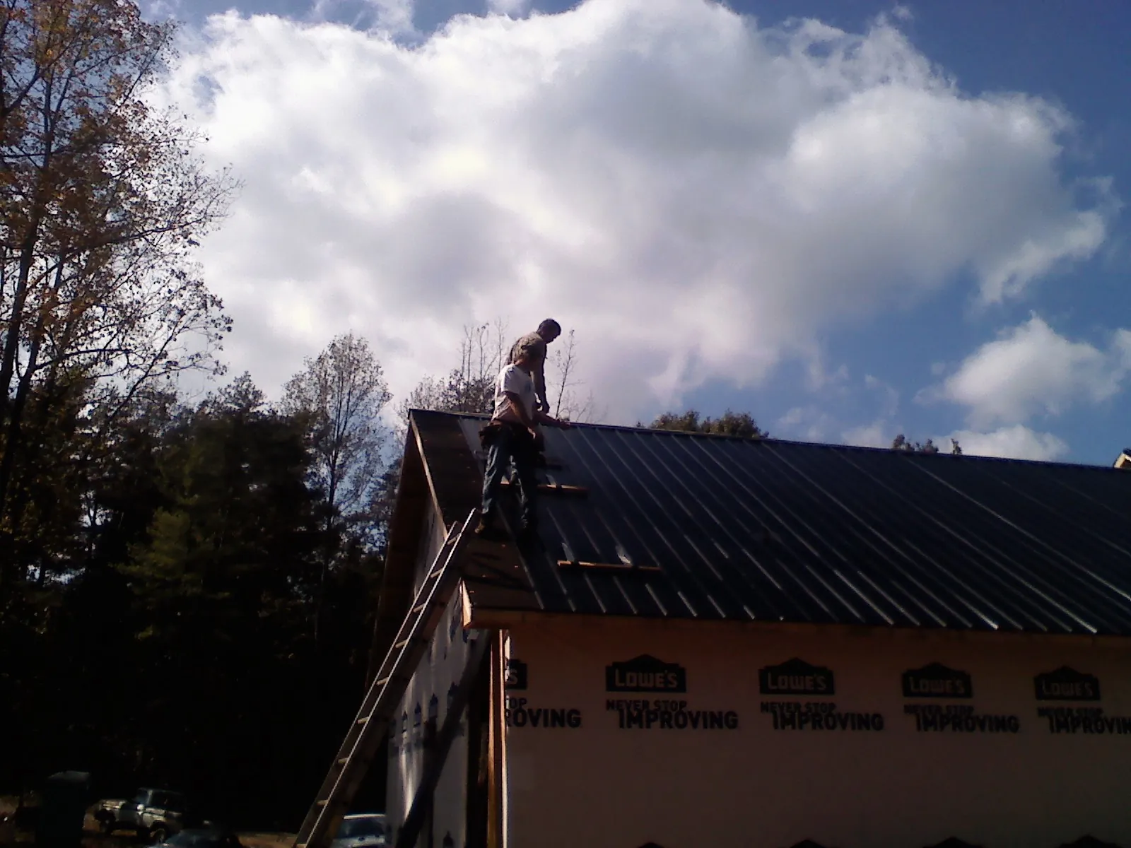 Roofer fastening dark metal panels high against a cloudy sky, from a Roof Inspection job in Bishop Hill