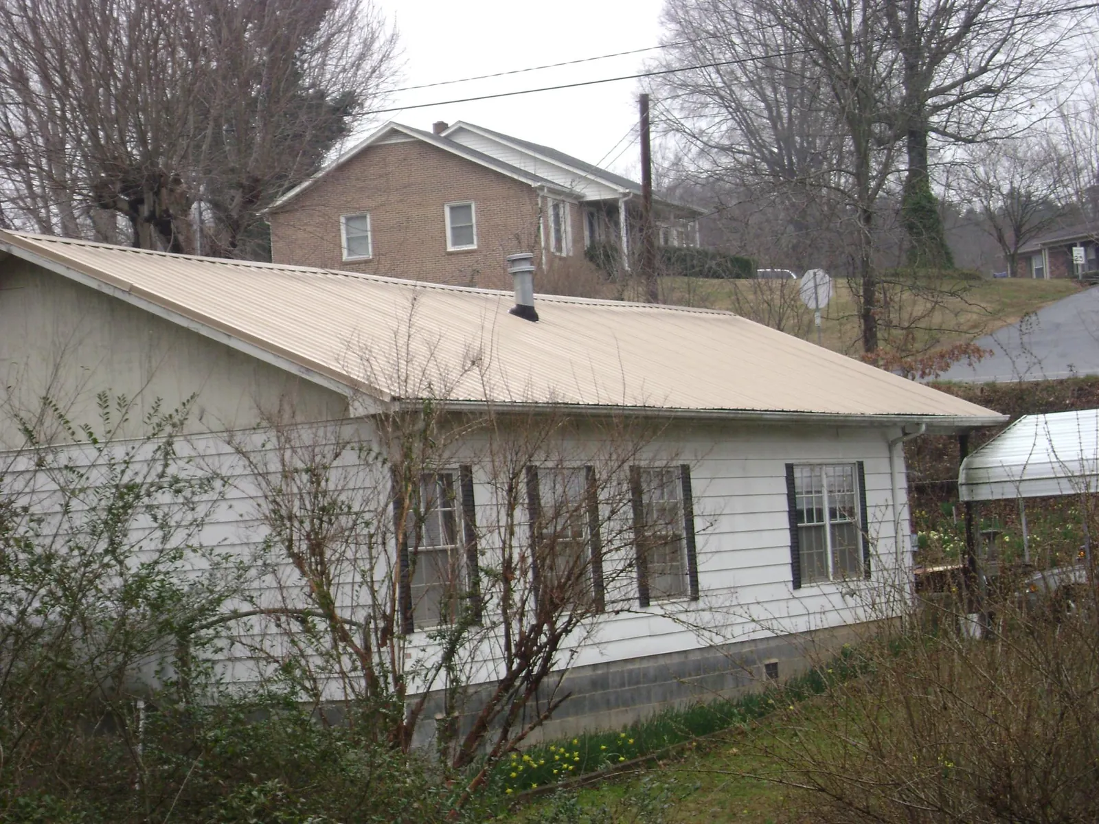 Tan metal roof on a white sided house set into a hillside — Commercial Roofing by Roofing Brothers in Bishop Hill