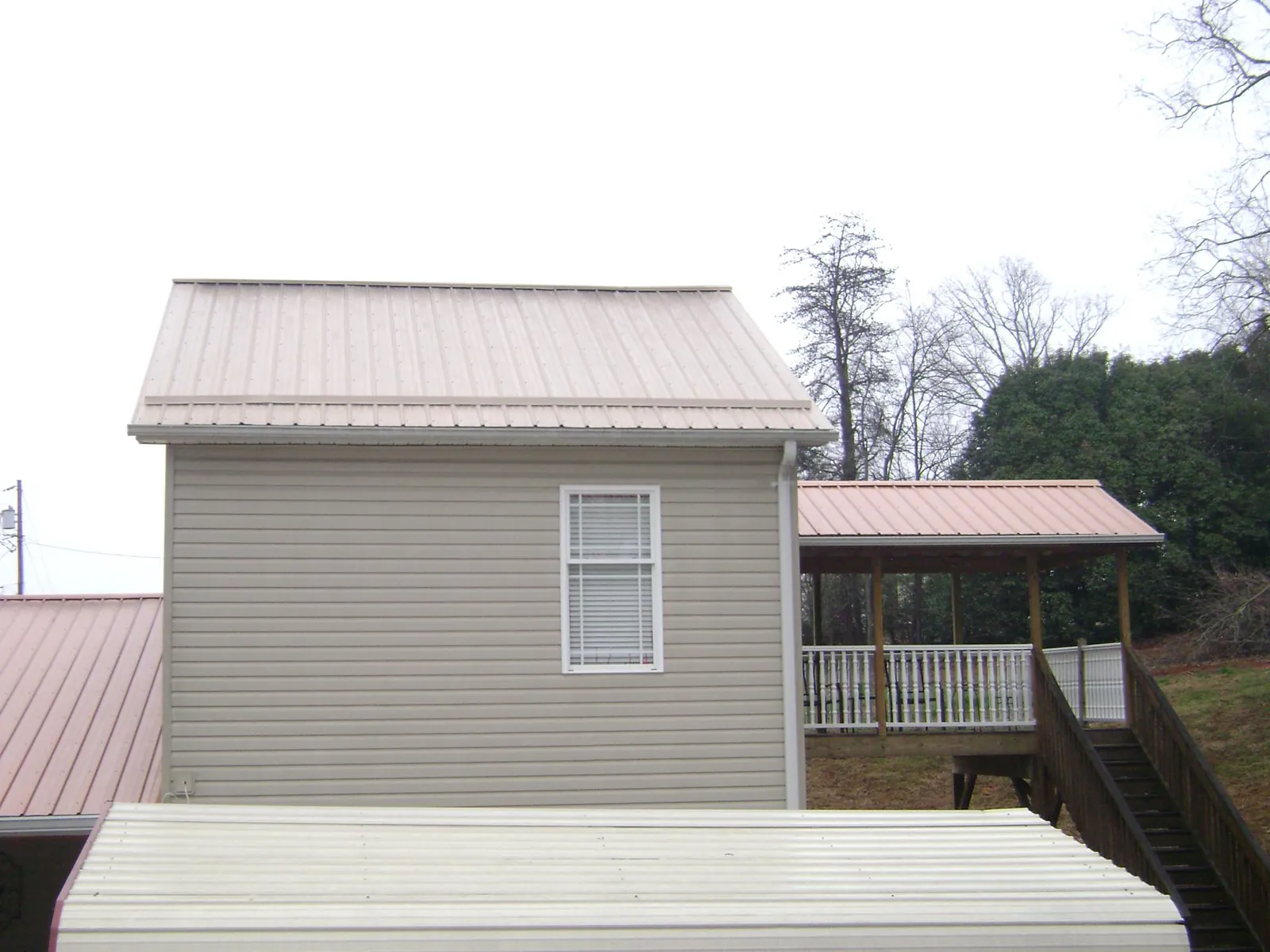 Tan metal roofs on a two story addition and attached porch, from a Roof Replacement job in Bishop Hill